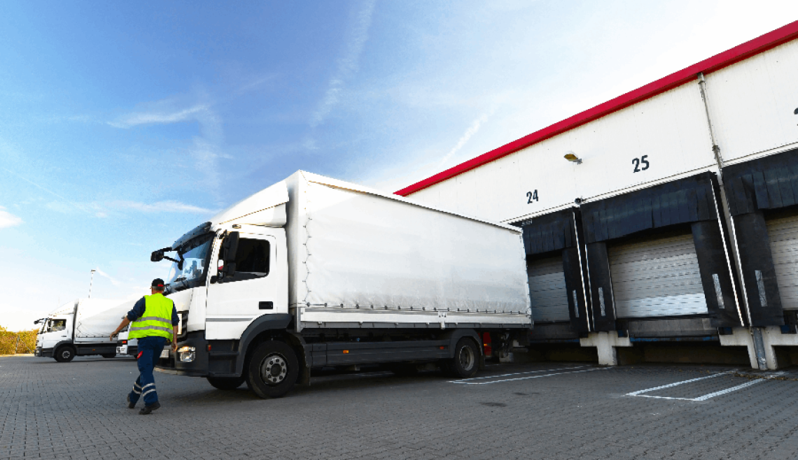 A truck is parked at a loading dock with workers nearby.