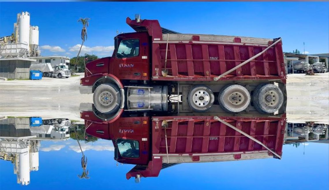 A red dump truck reflected perfectly in calm water.